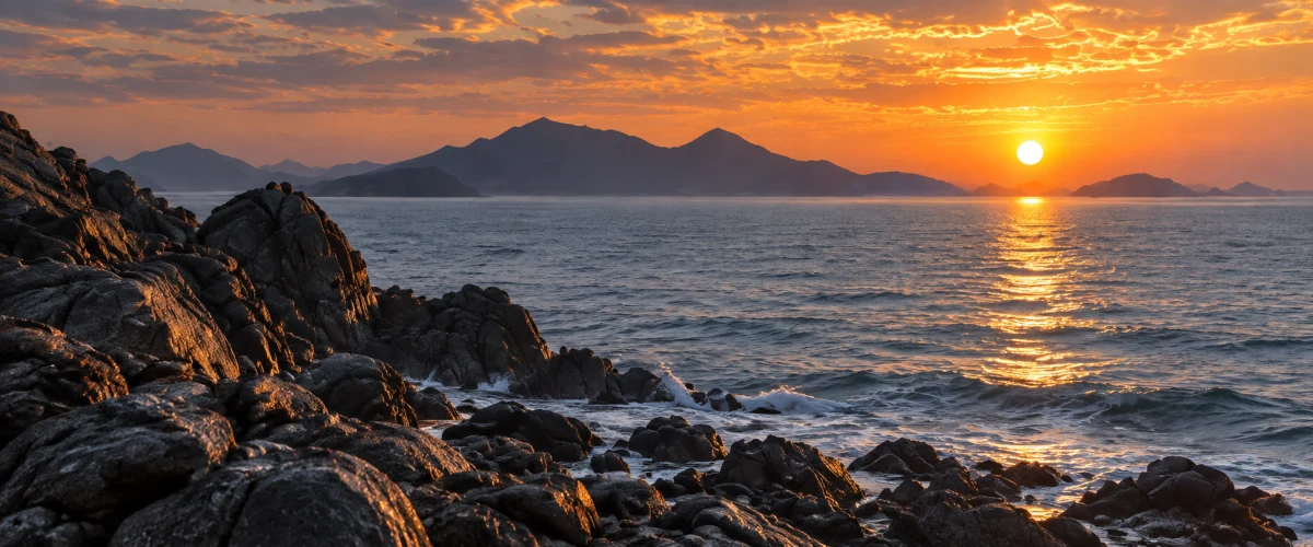 The sun sets over a rocky coast and distant mountain islands